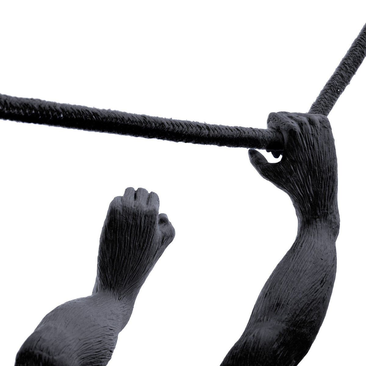 Close-up of a black sculpted monkey arm and hand gripping a textured black rope against a white background.
