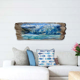 Wooden wall art shaped like driftwood with a painted blue and white glacier scene, mounted above a beige sofa with blue and fish-patterned pillows.