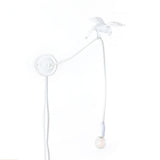 White wall lamp with a slender curved arm ending in a perched sparrow figure and a hanging exposed light bulb below it.