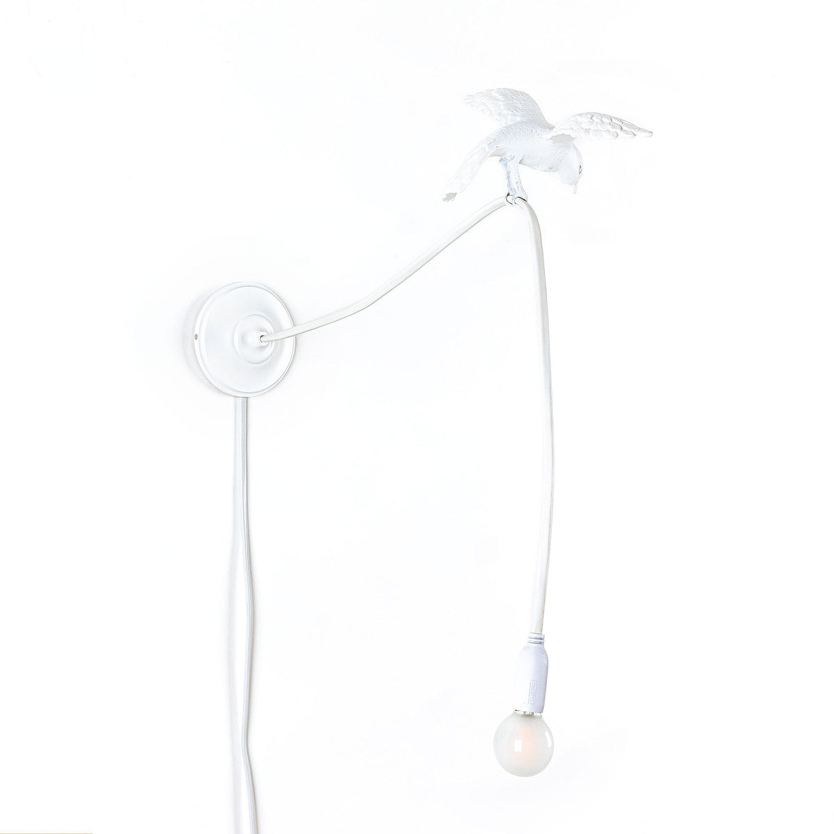 White wall lamp with a slender curved arm ending in a perched sparrow figure and a hanging exposed light bulb below it.