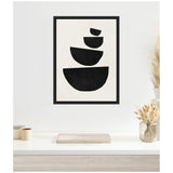 Framed abstract canvas with four irregular black semicircles stacked vertically against a white background, displayed on a white wall above a table with neutral decor.