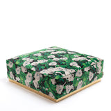 Square pouf with white rose and green leaf pattern covering fabric and a thin gold band around the base, shown against white background.