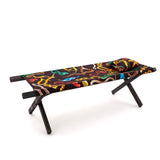 Bench with angled black wooden legs and a black fabric seat featuring a colorful abstract snake pattern including red, yellow, blue, green, and brown shapes, shown on white background.