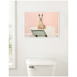 Framed canvas of a light brown llama sitting upright in a vintage clawfoot bathtub with a white towel, against a soft pink wall.