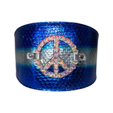 Wide blue leather cuff with textured finish and a silver band center, featuring a crystal-studded peace symbol attached on the front.