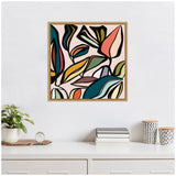 Framed abstract wall art featuring colorful, stylized overlapping leaves in shades of teal, orange, mustard, and black on a pale pink background above a white dresser.