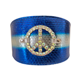 Wide blue metallic collar with a textured snakeskin pattern and horizontal white stripe, featuring a central rhinestone-studded peace symbol buckle.