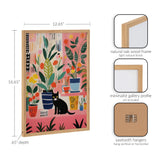 Framed colorful print showing a black cat sitting among various stylized houseplants in pots with a pink background, enclosed in a natural oak wood frame.
