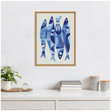 Framed blue canvas artwork featuring five stylized sardines with abstract geometric patterns, displayed above a white dresser with plant and books.