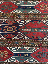 Close-up of an antique tribal cradleface textile featuring geometric patterns in red, blue, green, and beige with horizontal stripes and intricate motifs.