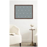 Rectangular pinboard with muted blue fabric featuring a repeating white botanical block print pattern, framed in dark wood, mounted above brass side table with white vase.