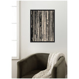 Abstract black and white vertical lines print framed in black, hanging on a white wall above an olive green chair draped with a cream knitted blanket.