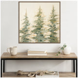 Abstract painting of three greenish evergreen trees with blurred brushstrokes on a light background, framed and hanging above a wooden table with books, a mug, and a white vase with greenery.