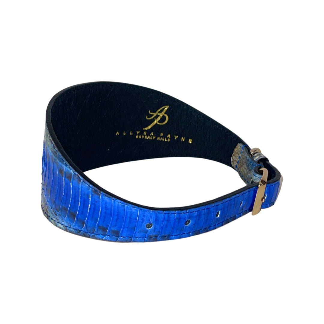 3-inch wide blue snake-patterned collar with gold-tone buckle and black interior lining featuring gold logo text, shown in a curved position on white background.