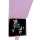 Poodle-shaped brooch with black resin legs and body, clear rhinestone-covered head, tail, and joints, displayed in an open pink box with black interior.