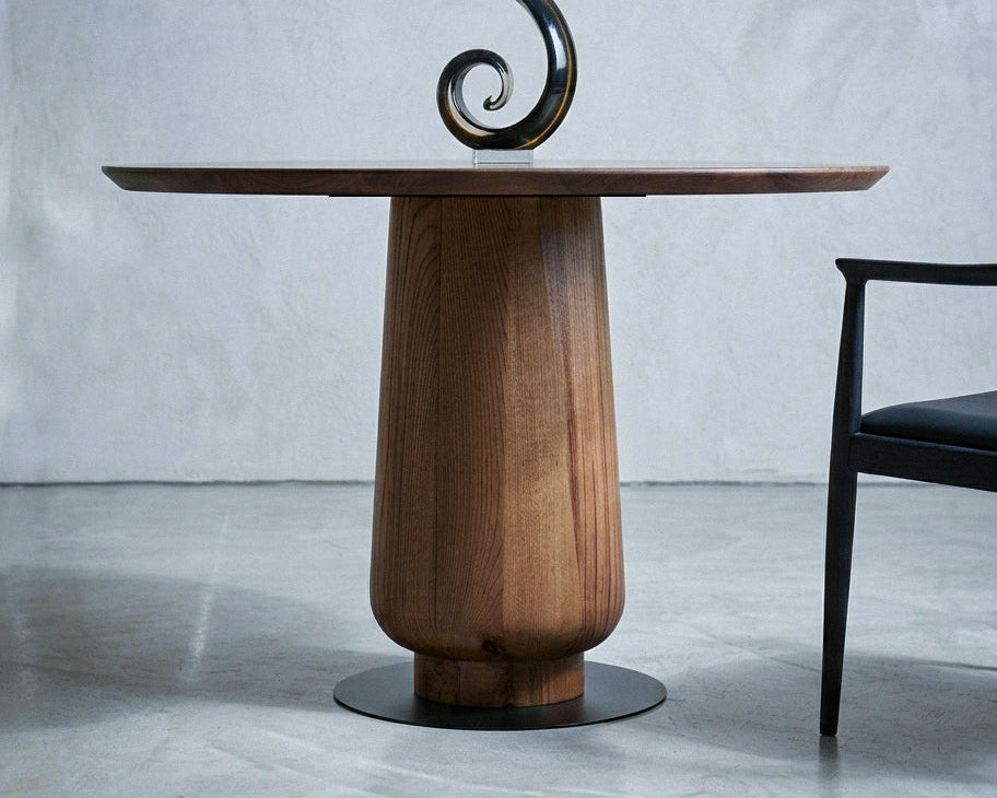 Modern round walnut dining table with sculptural pedestal base in a minimalist room