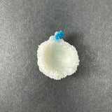 Small white Stilbite mineral with a textured, hollow center topped by a bright blue Cavansite ball, displayed on a dark gray background.