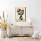 Framed abstract retro-style vase with colorful geometric sunflowers in pink, blue, orange, and yellow, hanging above a rustic wooden console in a bright minimalist room.