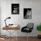 Minimalist office setup with a wooden desk, black adjustable lamp, and black chair with metal legs, decorated with framed black-and-white prints of tiger and moon phases on gray wall.