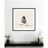 Black sketch-style bird perched on a horizontal branch, centered in a square white mat with a black frame, hanging on a white wall above a black surface with decor.
