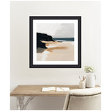 Framed abstract coastal landscape painting with tan sand, dark cliffs, and a muted blue horizon, displayed above a minimalist wooden desk and beige chair.