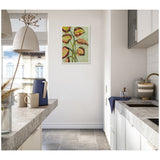 Vibrant foliage painting with abstract green, yellow, and red leaves on a light green background, framed and hung on a bright, modern kitchen wall.