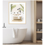 Framed print of three penguins in a white clawfoot bathtub with tropical palm leaves in the background, hanging above a white modern bathtub with a towel on its edge.