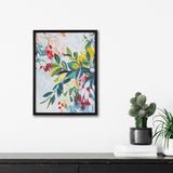 Framed botanical abstract art with colorful leaves and flowers, featuring shades of green, red, yellow, and blue on a light background, hanging above a black cabinet.