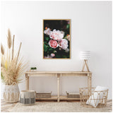 Framed canvas art featuring close-up of light and soft pink roses with green foliage, hanging above a rustic wooden console in a neutral-toned room.