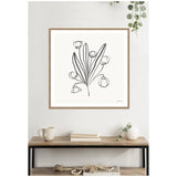 Framed minimalist black line drawing of a floral bouquet with long leaves and six flowers on a white background, hung above a wooden table with neutral decor.
