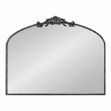 Arched rectangular wall mirror with dark metal frame featuring an ornate symmetrical floral motif at the top center, shown against a white background.
