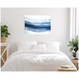 Framed Abstract Linear Blues canvas print with flowing horizontal blue and white waves, hanging above a white bed in a minimalist room with green plants.