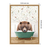 Brown bear resting its head on the edge of a green clawfoot bathtub filled with bubbles, set against floral wallpaper and white wainscoting on a wood floor.