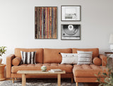 Three framed canvas prints above a caramel leather sectional sofa: vertical rows of colorful vinyl records, a black and white line drawing of a record player, and a monochrome photo of a spinning vinyl record.