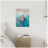 Framed aerial photo of a beach with turquoise water, colorful umbrellas, and a rocky outcrop extending into the sea, hanging on a white bedroom wall above a wooden bedside table.