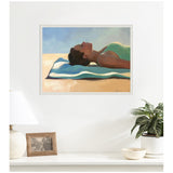 Framed painting of a woman lying on her back on a beach towel, wearing a green top, against a blue sky background, displayed above a white shelf with a lamp, photo, and plant.