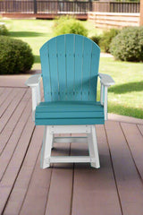 Swivel Adirondack chair with teal slatted back and seat, white armrests and base, positioned on a brown wooden deck with green bushes in the background.