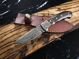 Damascus steel fixed blade knife with intricate wave patterns, featuring a dark walnut handle with brass accents, resting on a stitched brown leather sheath atop natural wood.