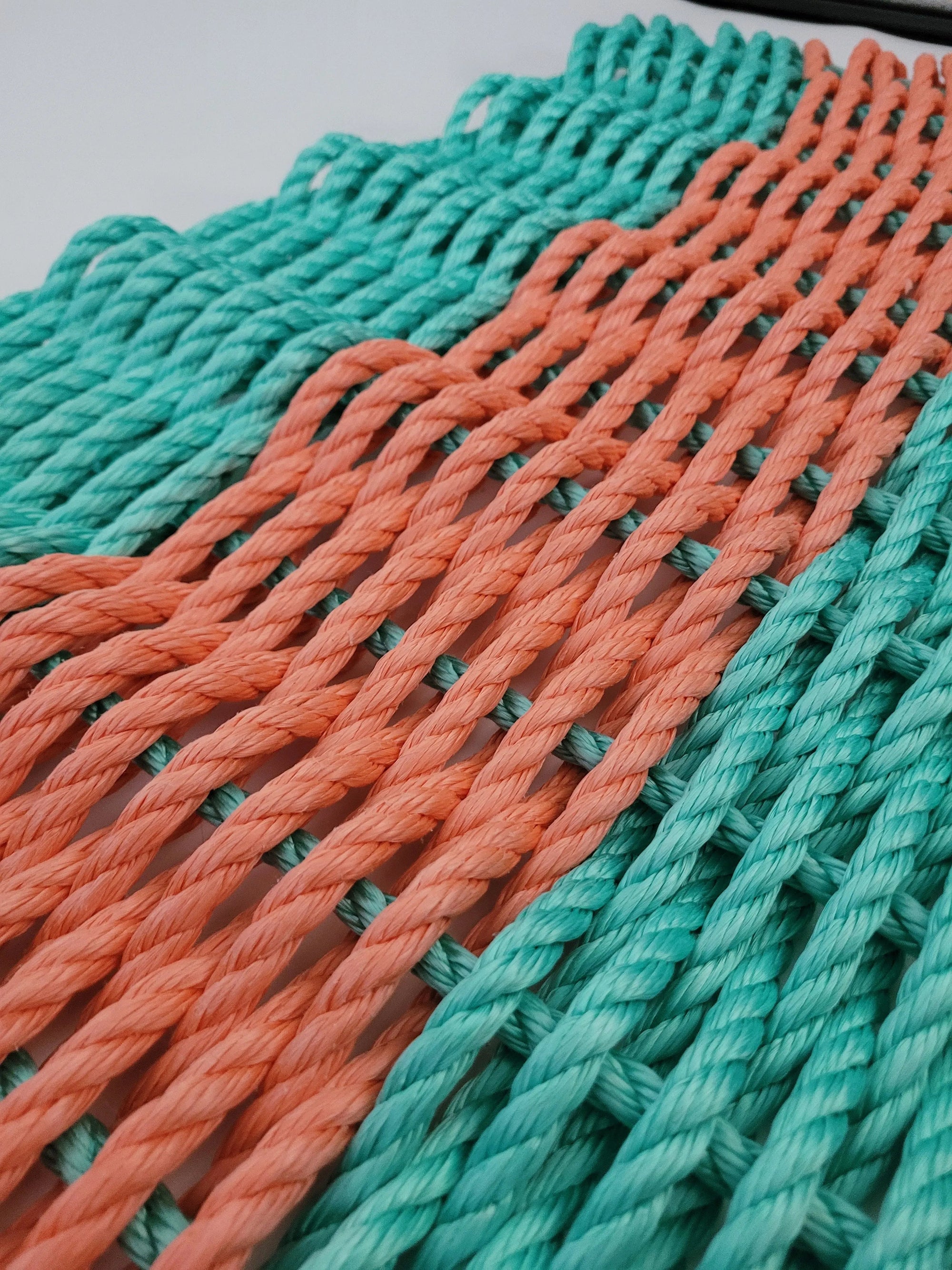 Handmade lobster rope mat in teal and coral orange on wooden floor