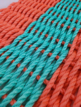 Handmade coral orange and teal lobster rope mat on wooden floor
