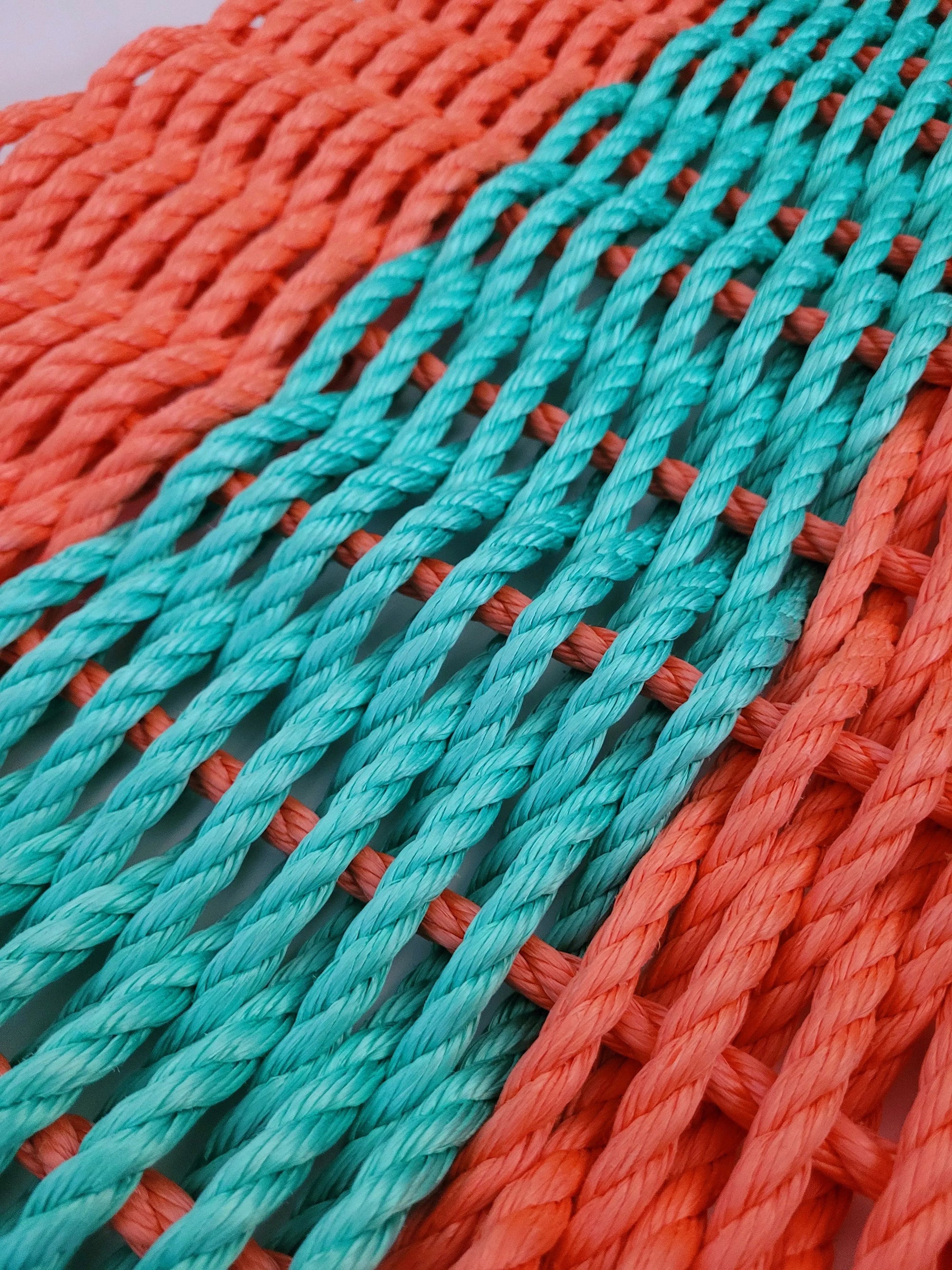 Handmade coral orange and teal lobster rope mat on wooden floor