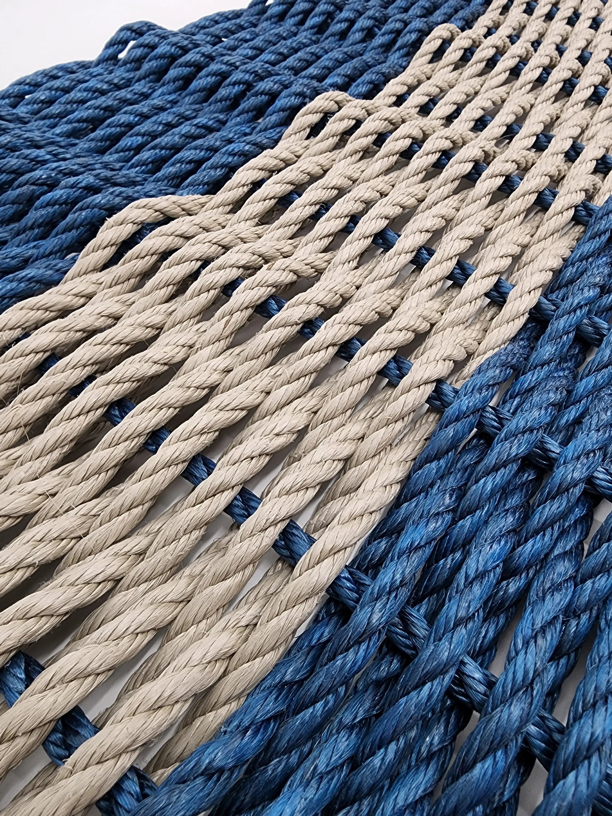 Handmade navy blue and tan lobster rope mat on wooden floor