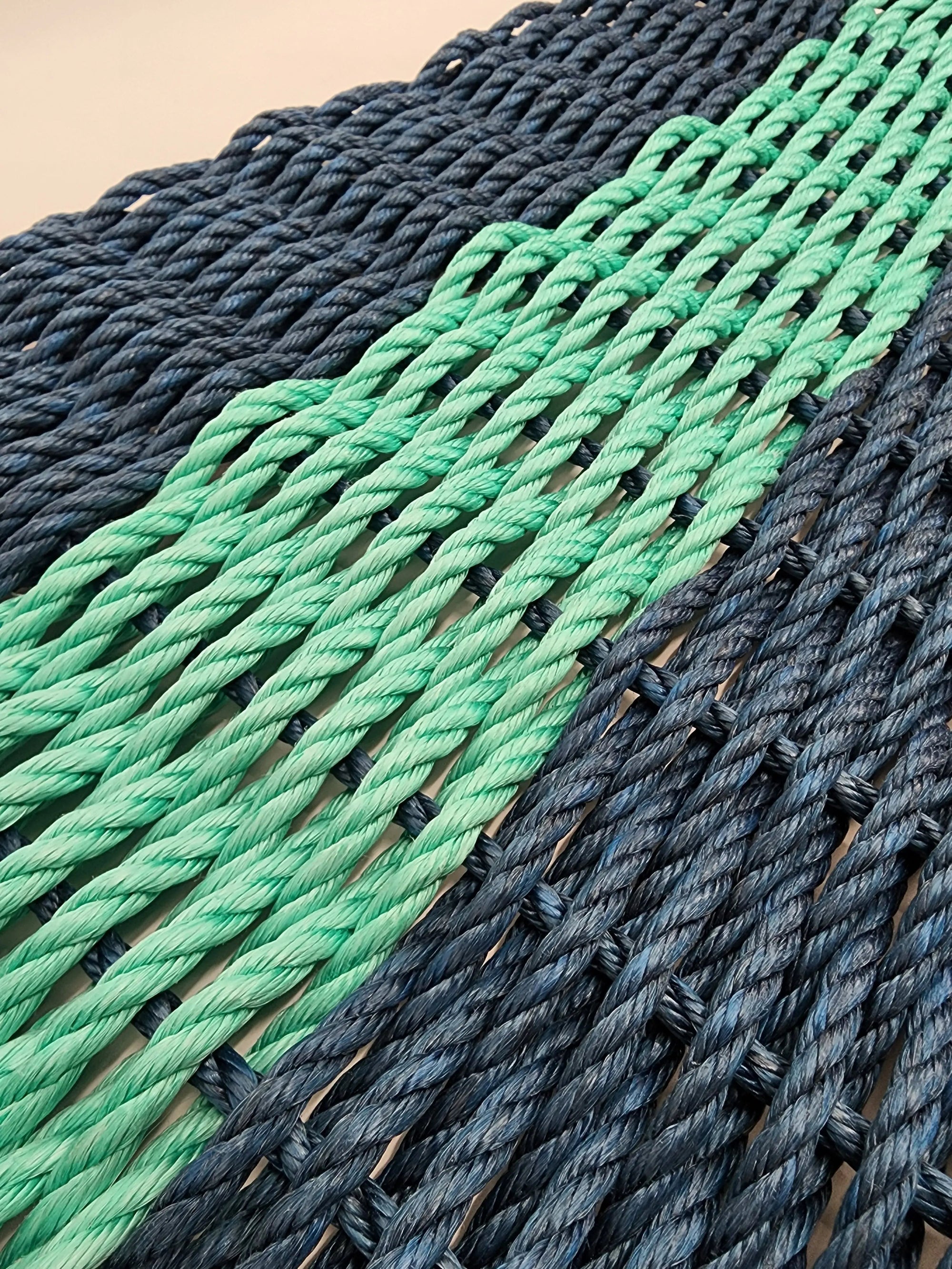 Handmade navy blue and teal lobster rope mat on wooden floor