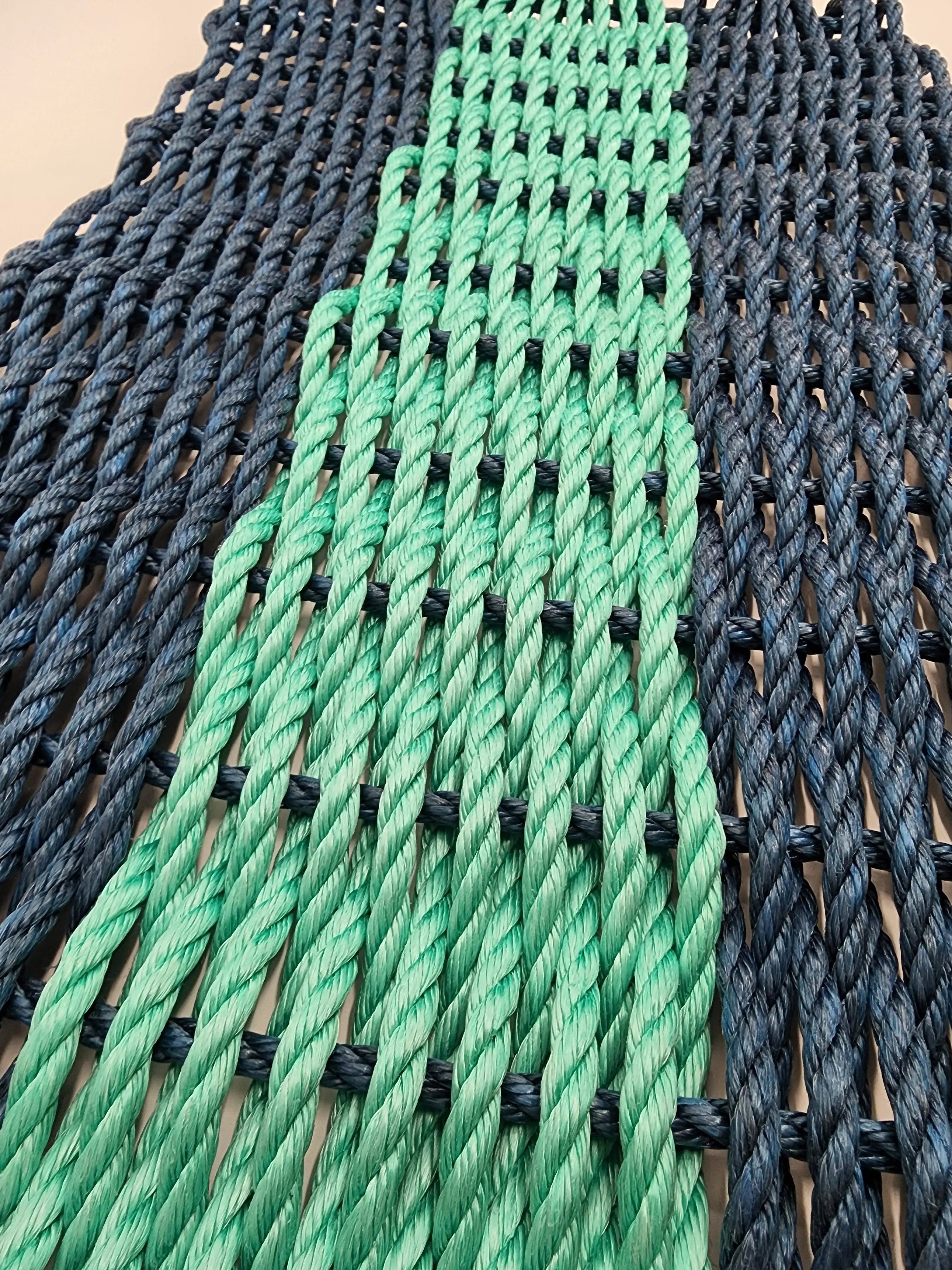 Handmade navy blue and teal lobster rope mat on wooden floor