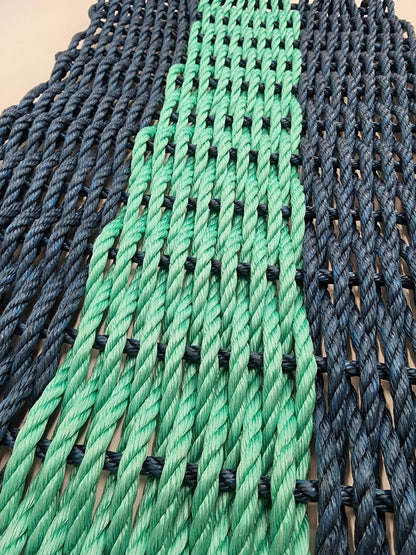 Handmade navy blue and teal lobster rope mat on wooden floor