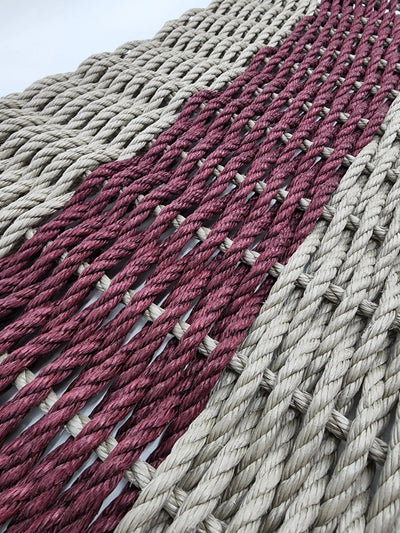 Handmade lobster rope mat in tan and burgundy colors on a wooden floor