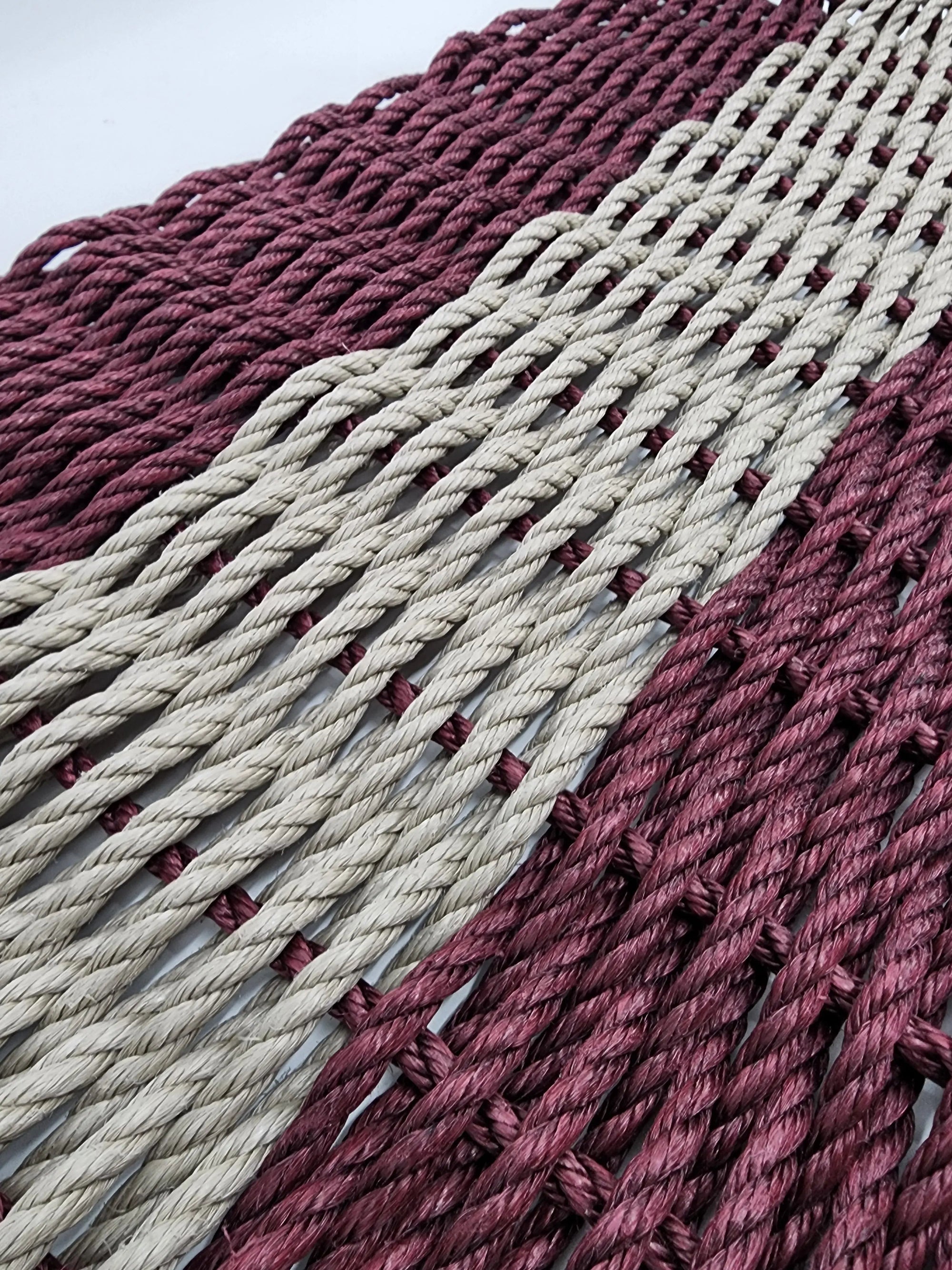 Burgundy and tan handmade lobster rope mat on wooden floor