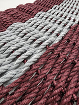 Handmade burgundy and light gray lobster rope mat on wooden floor
