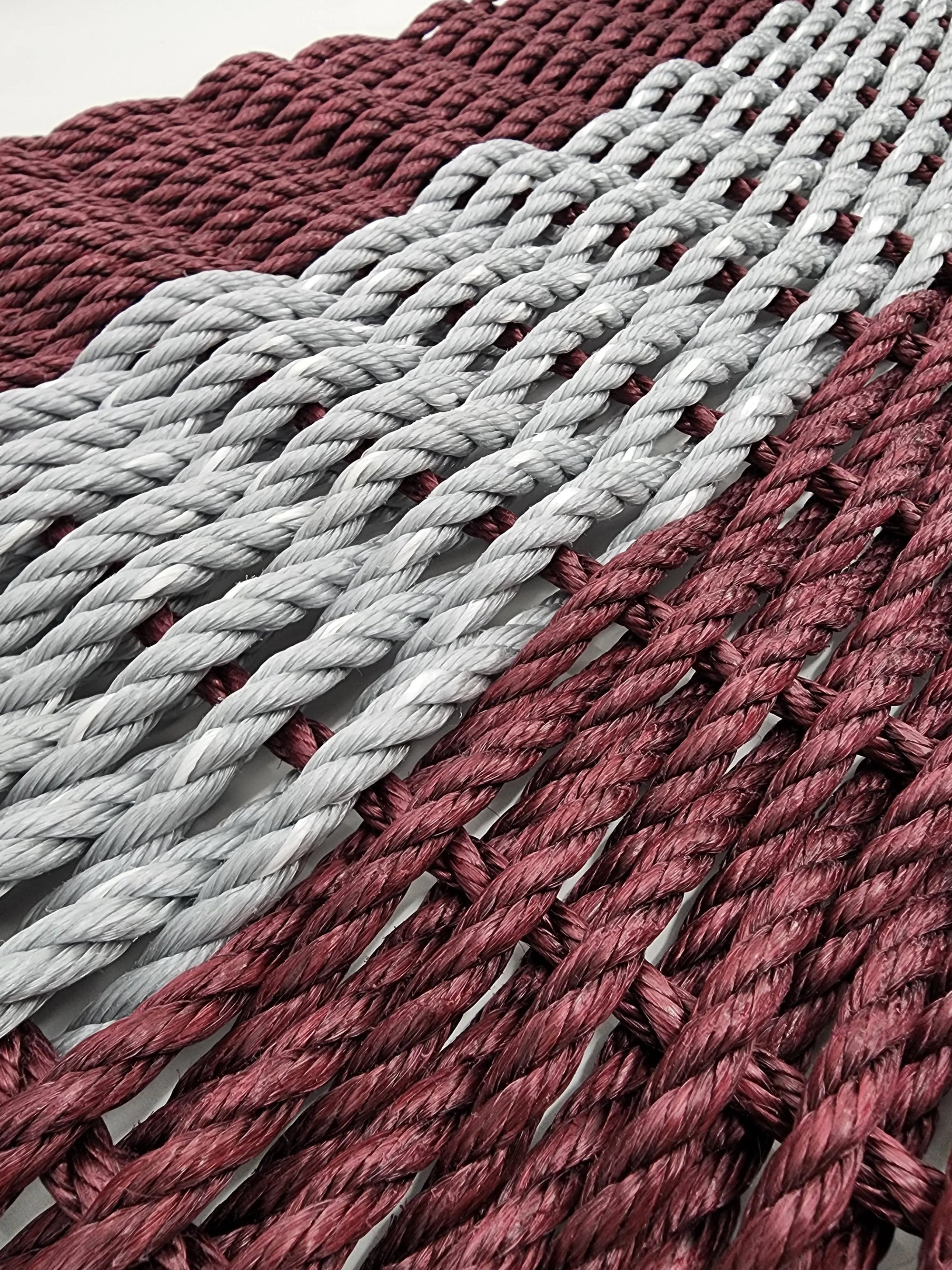 Handmade burgundy and light gray lobster rope mat on wooden floor