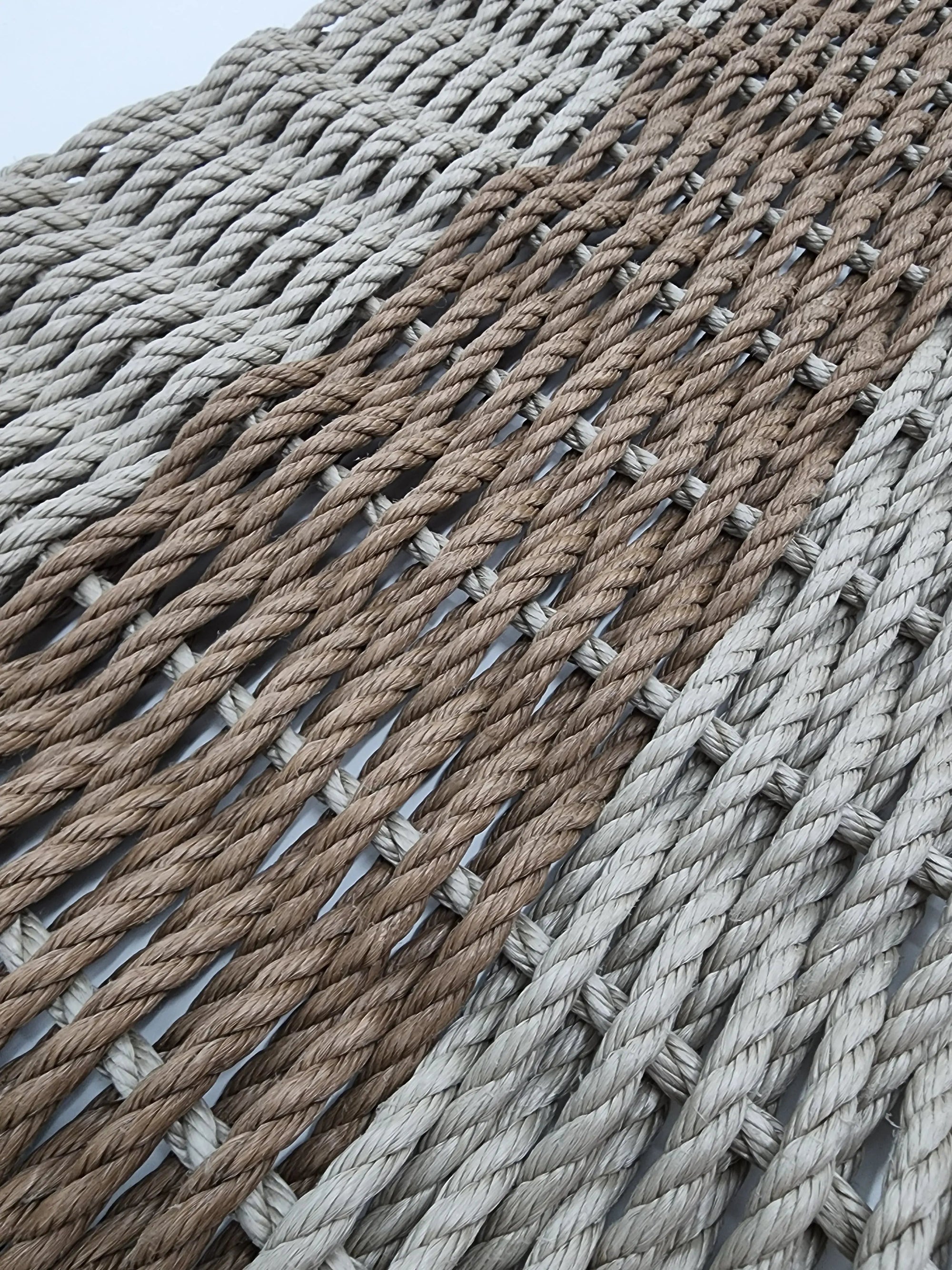 Handmade lobster rope mat in tan and brown colors, displayed on wooden floor